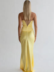 Woman wearing a yellow evening gown with a backless design on a plain background