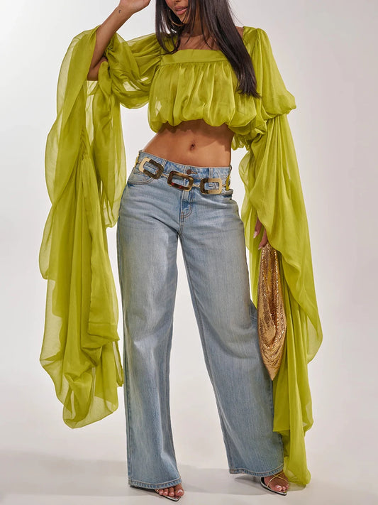 Lime green draped square neck crop top with wide-leg jeans and a gold chain belt.