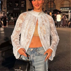 Woman wearing a white lace top and jeans on a city street.