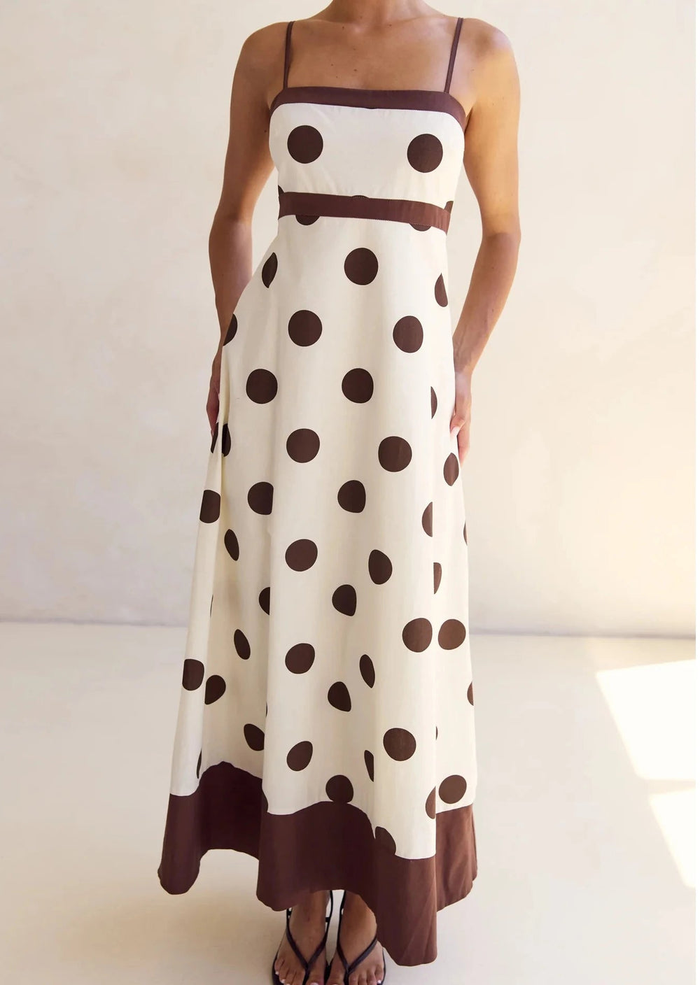 Woman wearing a polka dot dress with brown and white colors on a plain background