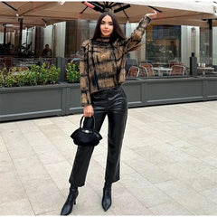 Woman in plaid sweater and black pants standing outdoors under an umbrella.