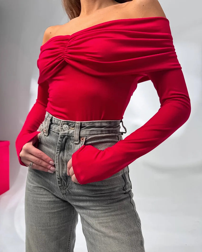 Person wearing a red off-shoulder top and gray jeans on a plain background