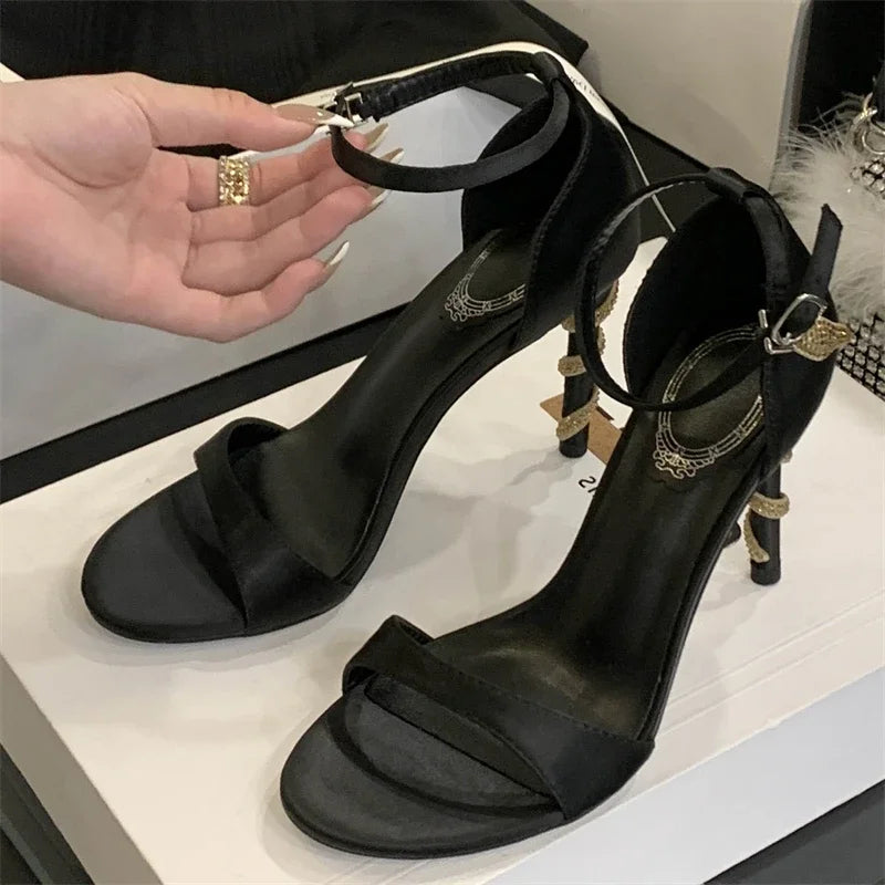 Black high-heeled sandals with decorative straps on a white surface.