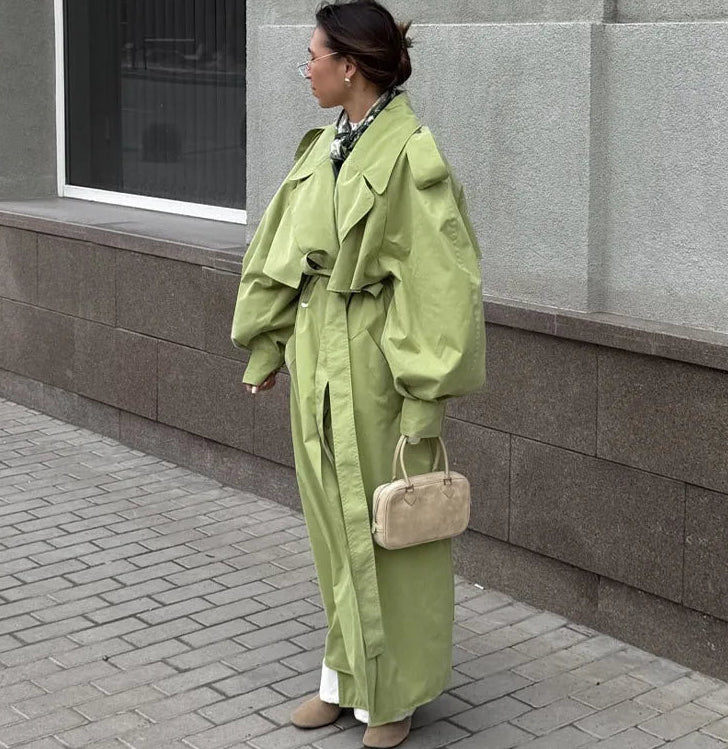 Person wearing a long green coat standing against a gray building.