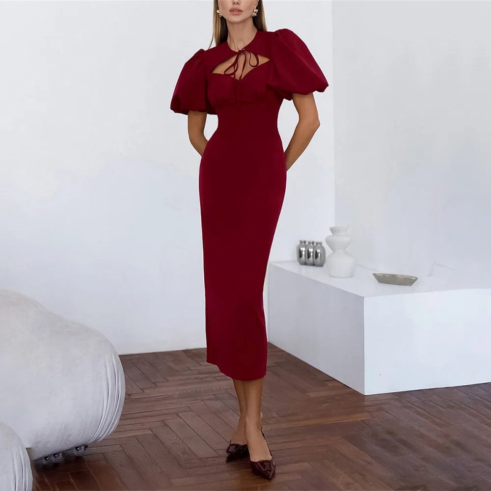 Woman wearing a burgundy dress with puff sleeves in a minimalistic room.