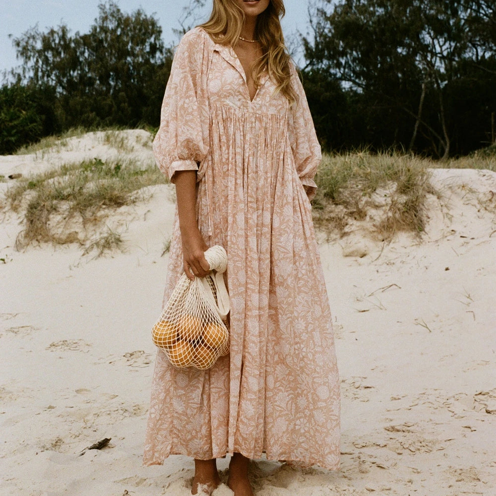 Blonde model wearing a pink floral print maxi dress on a beach