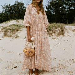 Blonde model wearing a pink floral print maxi dress on a beach