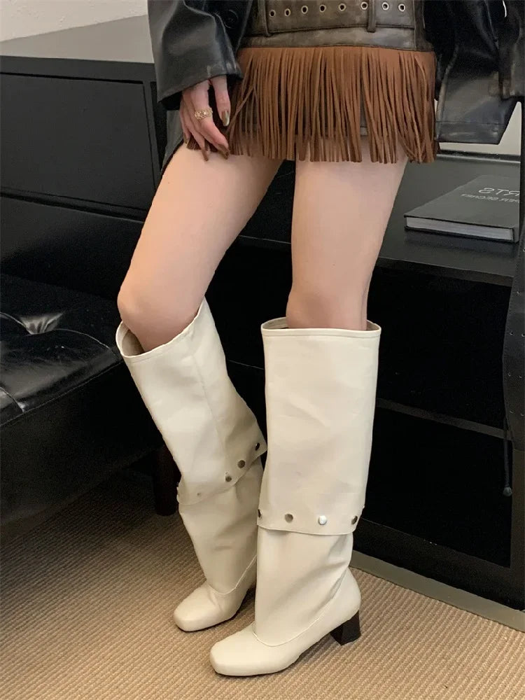 Person wearing white knee-high boots with a fringe skirt in an indoor setting