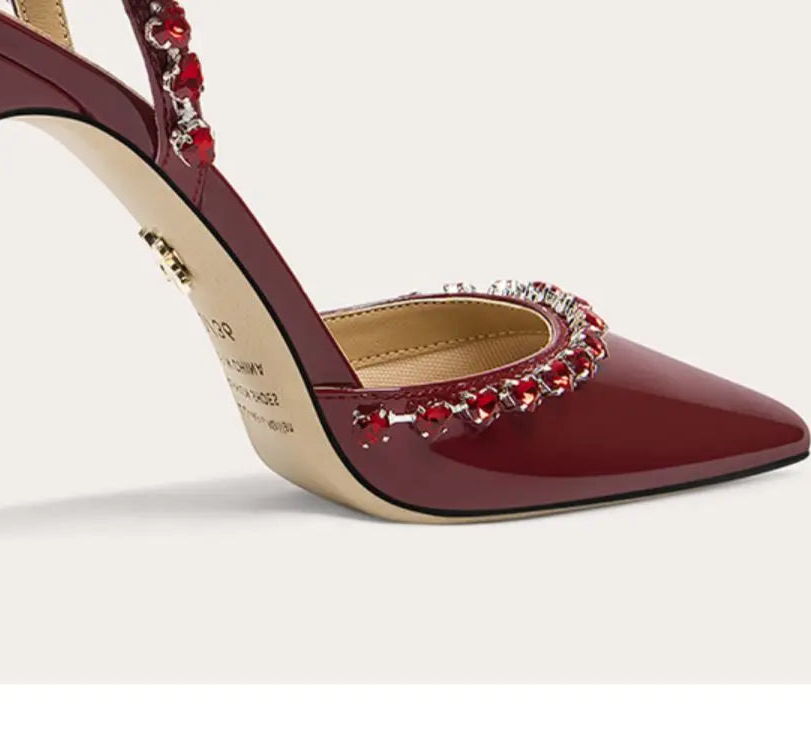 Maroon high-heeled shoe with decorative red embellishments on a light gray background