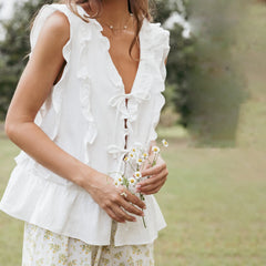 Woman wearing a white ruffled top and floral skirt holding flowers outdoors.