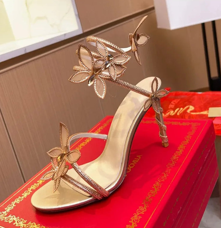 Gold high-heeled shoe with butterfly decorations on a red surface.
