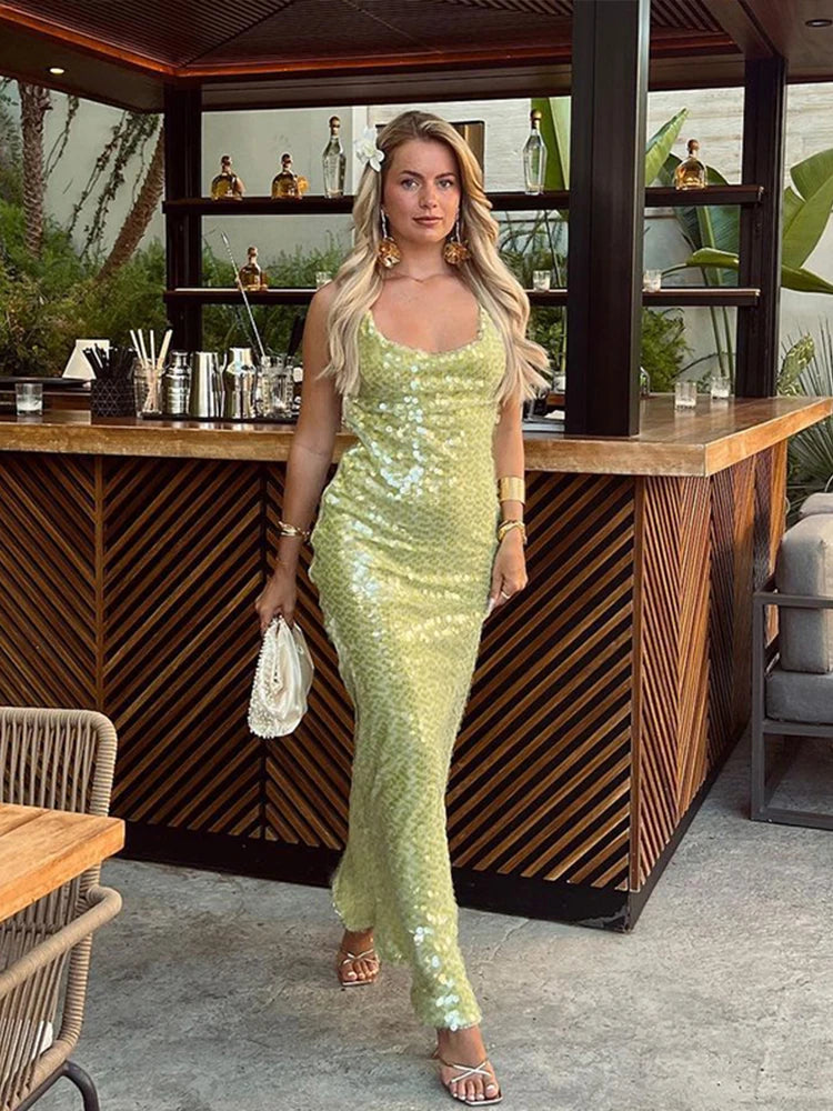 Woman in a green sequin dress standing in front of a bar counter.