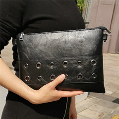 Person holding a black leather clutch with grommet details