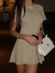 Woman wearing a beige dress holding a white handbag indoors.