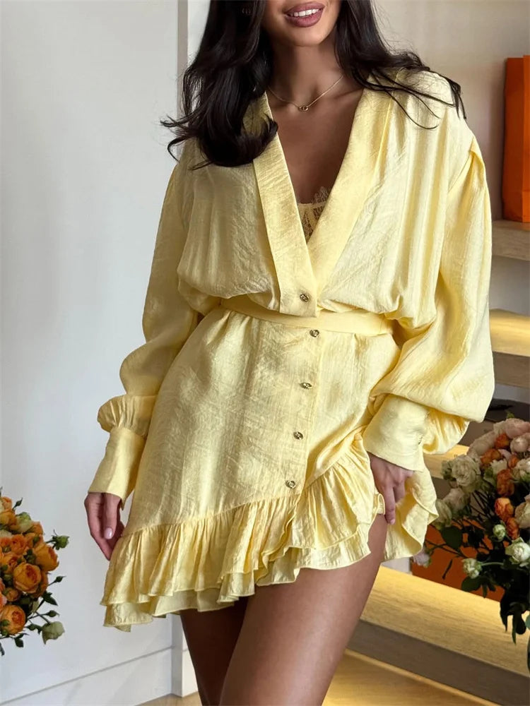 Woman wearing a yellow dress with long sleeves and ruffled layers in an indoor setting.