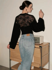 Person wearing a black lace top and light blue jeans in a room with a wooden cabinet.