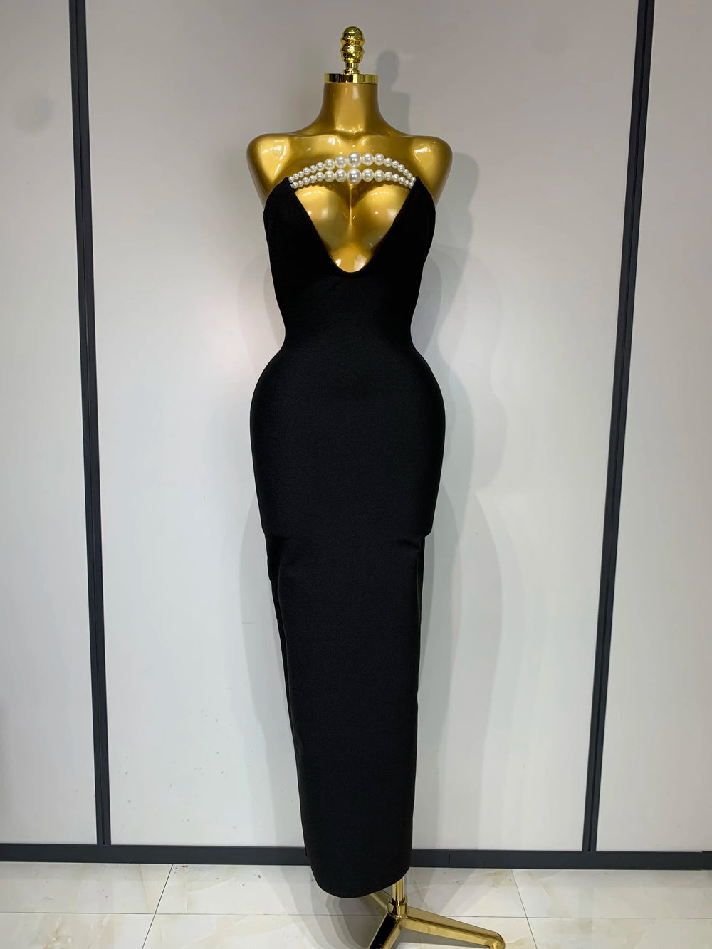 Black evening gown on a mannequin with pearl embellishments against a white background