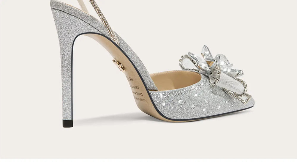 Silver glitter high-heeled shoe with a decorative bow on a light gray background
