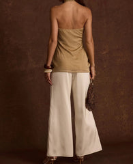 Woman wearing a beige top and white pants against a brown background