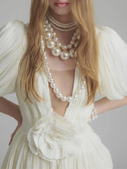 Woman wearing a white dress with a large pearl necklace against a gray background
