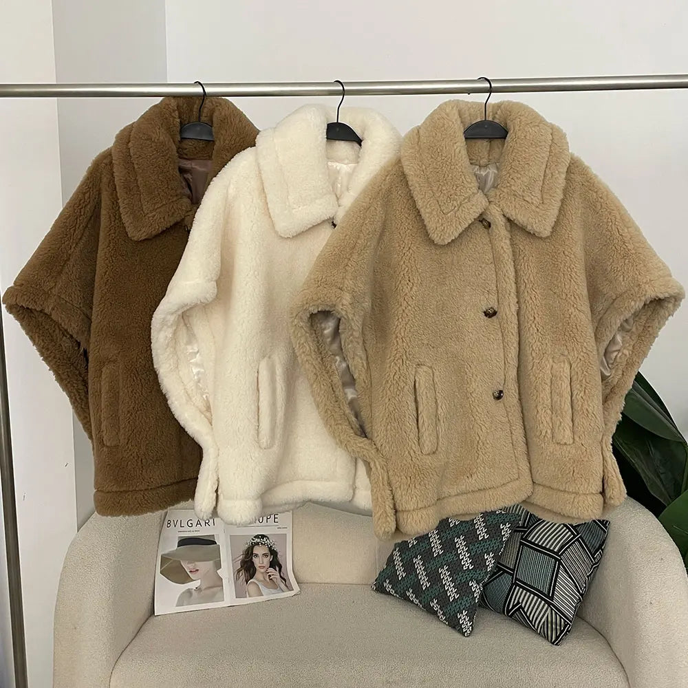 Three sheepskin jackets in brown, white, and beige hanging on a rack against a white wall.