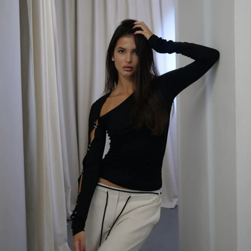 Woman wearing a black top with cut-out design and white pants against a white curtain background