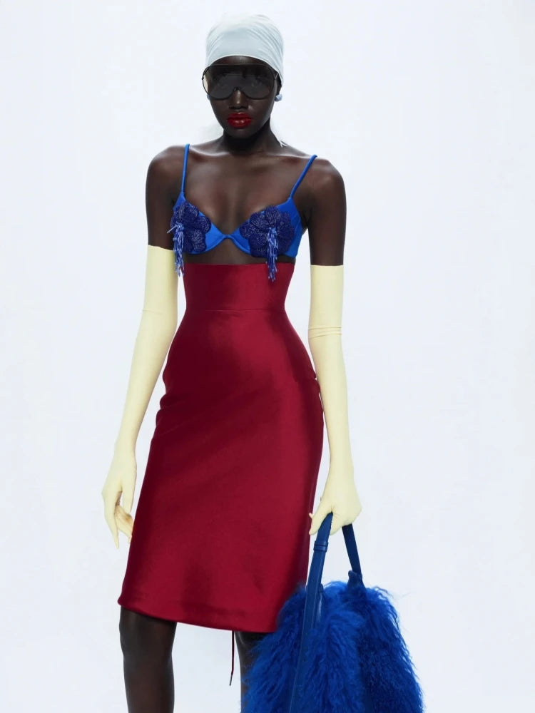 Model wearing a red dress with a blue lace top and white gloves, holding a blue feathered bag on a white background.