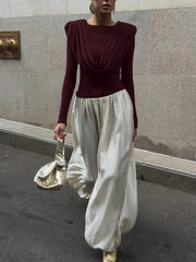 Person wearing a burgundy top and white pants against a stone wall.