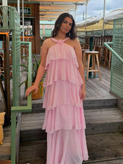 Woman wearing a pink dress standing on a wooden deck with outdoor furniture in the background