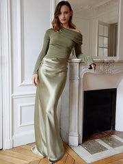 Woman in a green off-shoulder top and satin skirt standing in a room with a fireplace.