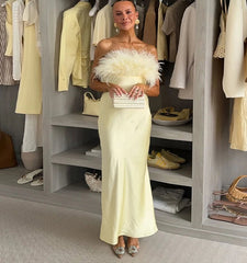 Woman in a light-colored evening gown with feathered top standing in a wardrobe filled with clothes and shoes.