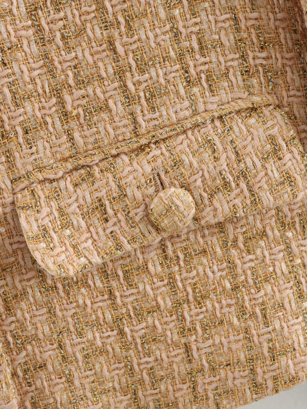 Close-up of textured fabric with a button, featuring a herringbone pattern.