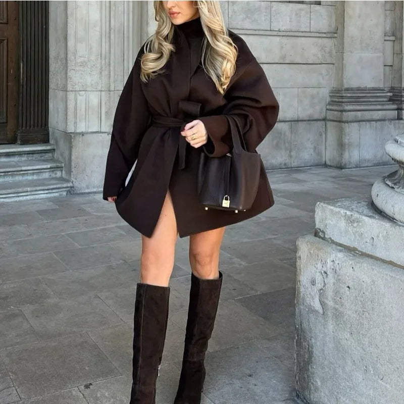 Woman wearing a brown coat and knee-high boots in an urban setting
