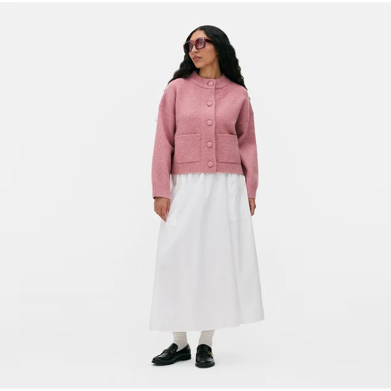 Woman wearing a pink cardigan and white skirt on a white background