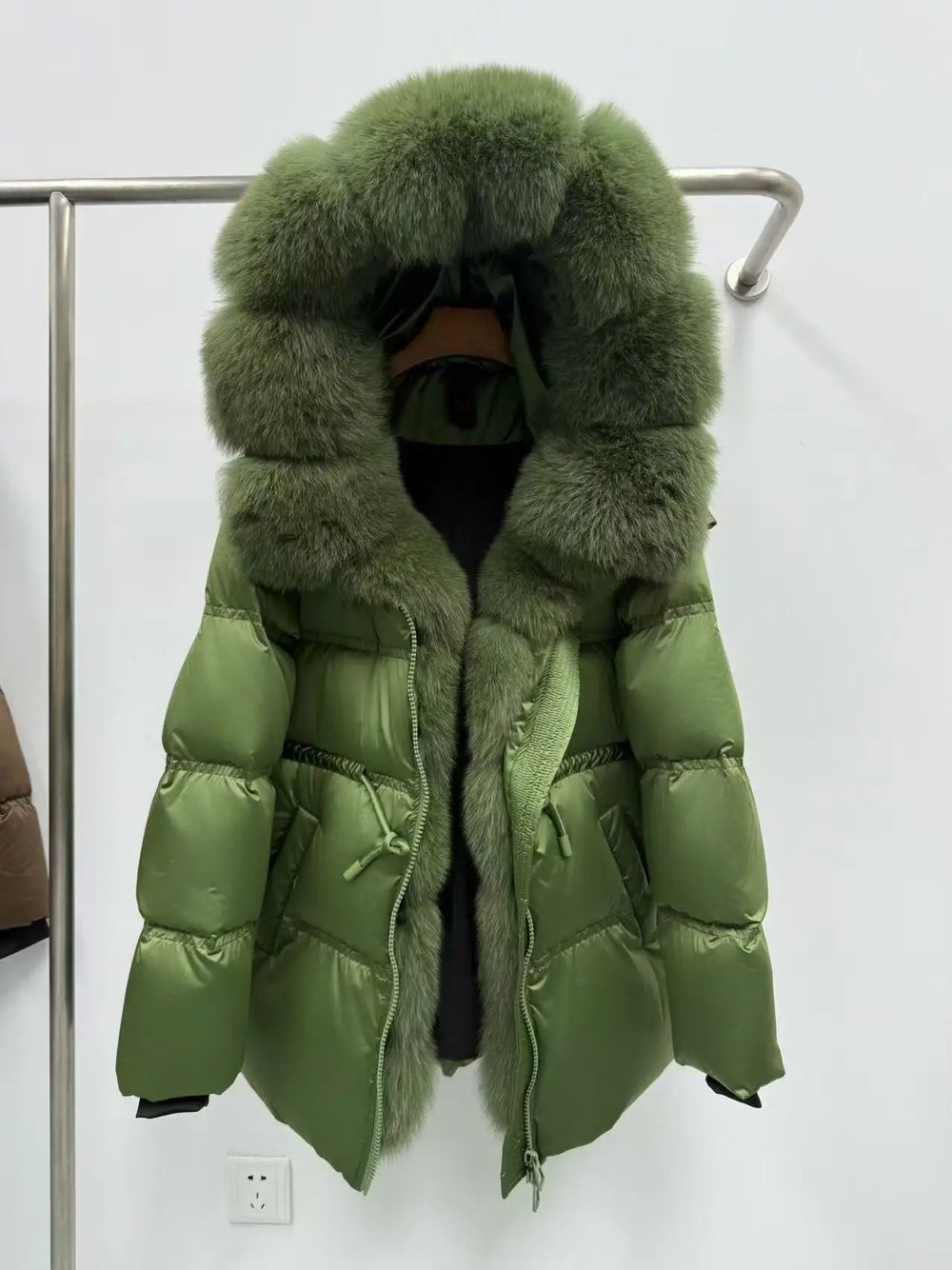 Green puffer jacket with fur hood on a rack against a white wall.