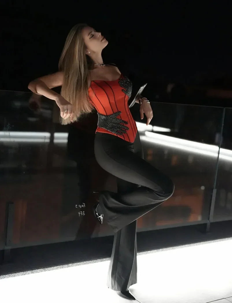 Woman in a red top and black pants posing against a dark background