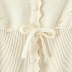 Close-up of a cream-colored ribbed knit cardigan with buttons and a tie detail.