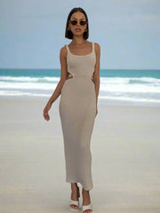 A woman wearing a light brown geometric patterned dress with an ankle-length, sleeveless design  standing in a beach.
