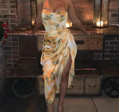  Golden Atelier tie-dye sundress with a relaxed silhouette and spaghetti straps. The dress features a colorful tie-dye pattern and is modeled on a woman in a summery setting. Yellow 2