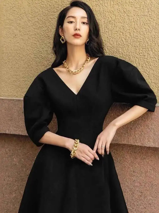 Model walking outdoors in a structured A-line dress, with a clean V-neck and full skirt movement along a cobblestone street.