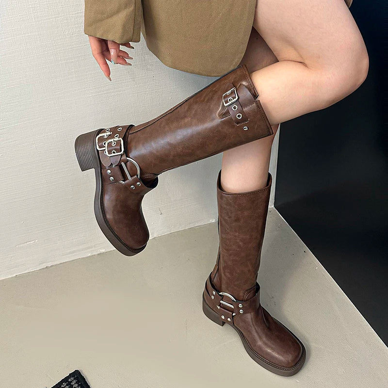 Anti-slip urban commute brown boots with a square toe and a block heel worn by a person sitting on a white surface.