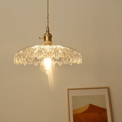 A hanging ceiling light with a transparent glass shade designed to resemble a flower, with a visible bulb and a metallic gold finish, and a painting on the back side.