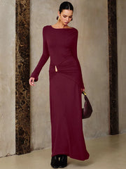 A woman wearing an elegant Autumn party knit gown in deep burgundy is shown for gala events against a textured wall.