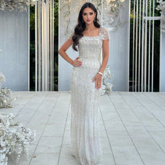 White mermaid beaded evening dress styled for Dubai weddings, white lace dress standing in a decorated outdoor setting with flowers.