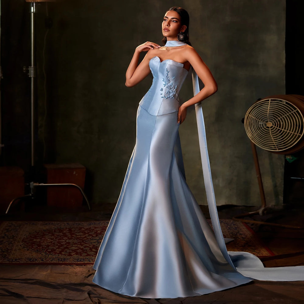 Woman in a light blue evening gown standing in a dimly lit room.