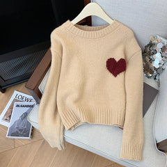 Beige sweater with red heart patch styled on chair