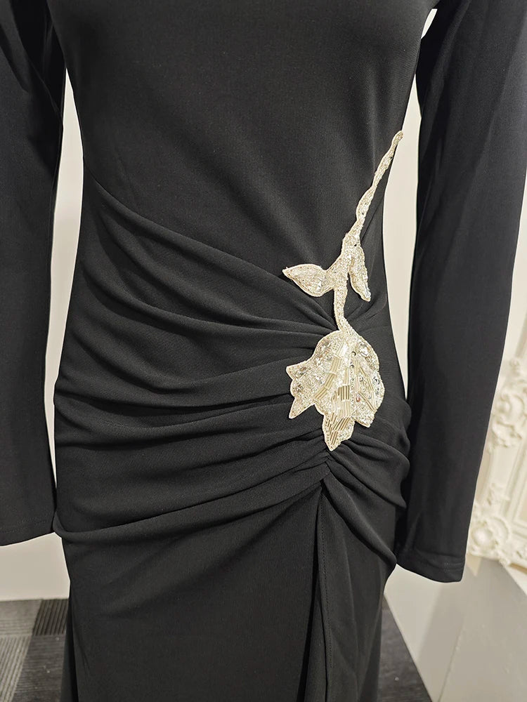 Close detail of the crystal floral embellishment at the hip on a black gown, highlighting the sculpted drape and gathered waist