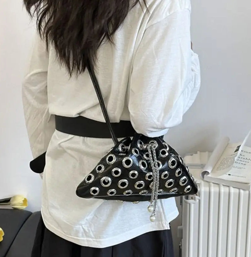 Close-up of metal eyelet rivets across the black bag, showing the glossy finish and hardware pattern in crisp detail.