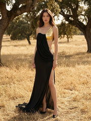 Full-length coastal scene showing a sleek black sheath gown with asymmetric neckline and soft drape across the bodice