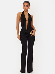 Model wearing a black halter plunge top with matching ankle-length trousers, posed against a white studio background with sleek evening styling.